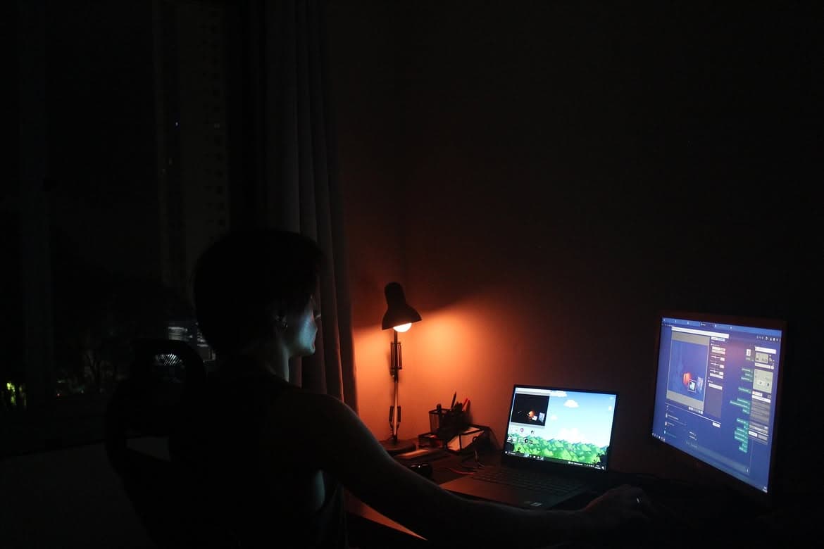 Pessoa de costas sentada à mesa à noite, iluminada por um abajur